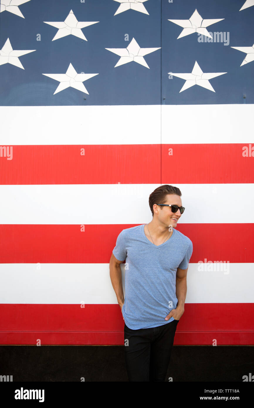 Junge Mann in den Taschen stehend gegen amerikanische Flagge tragen Sonnenbrillen mit Händen Stockfoto