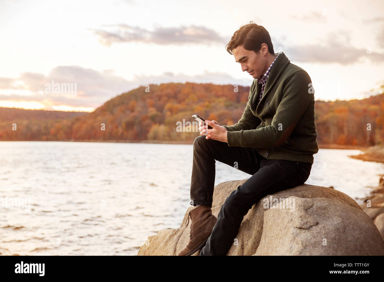 Mann mit Handy beim Sitzen auf Felsen am Seeufer Stockfoto
