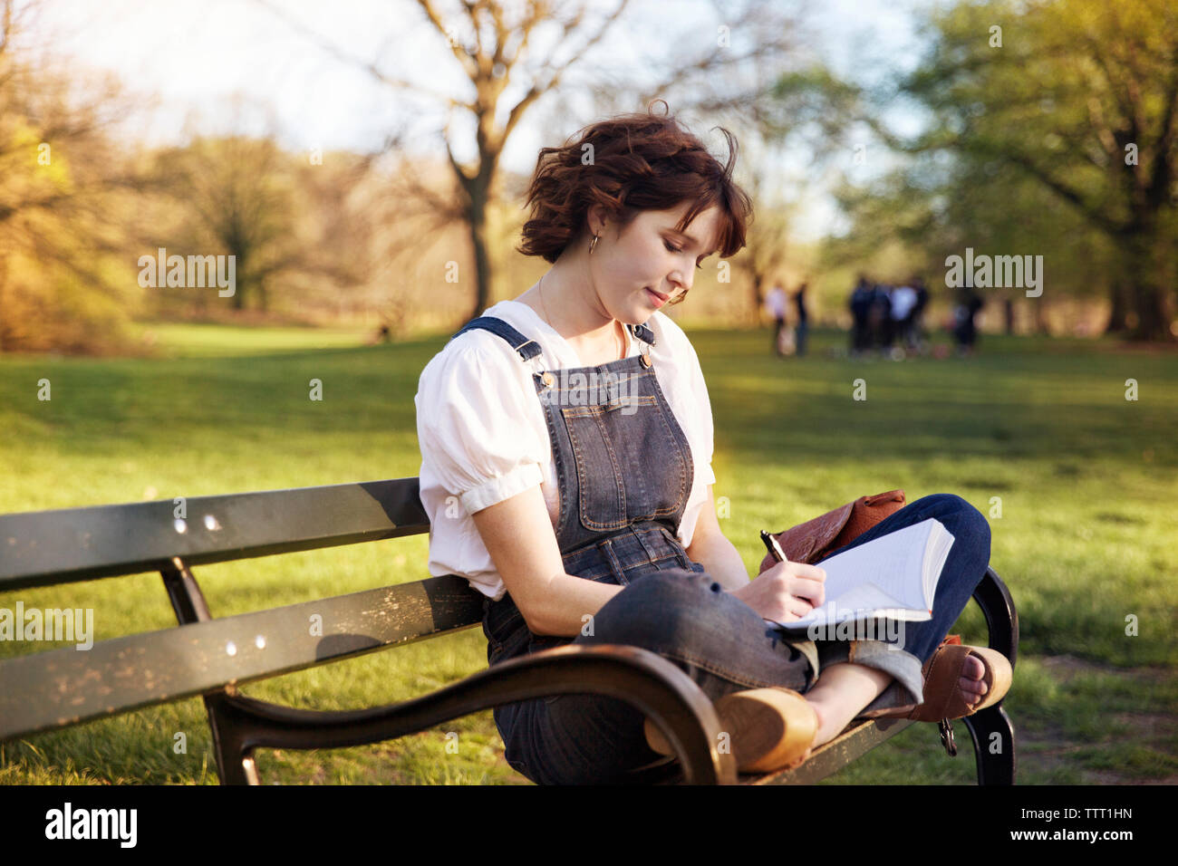 Frau mit cross-legged schriftlich beim Sitzen auf der Parkbank Stockfoto