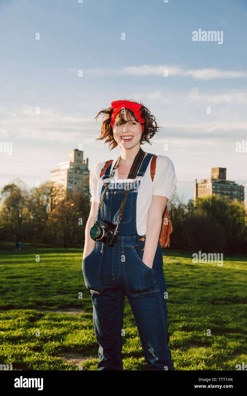 Glückliche Frau mit Händen in den Taschen auf der Wiese im Park gegen Sky Stockfoto