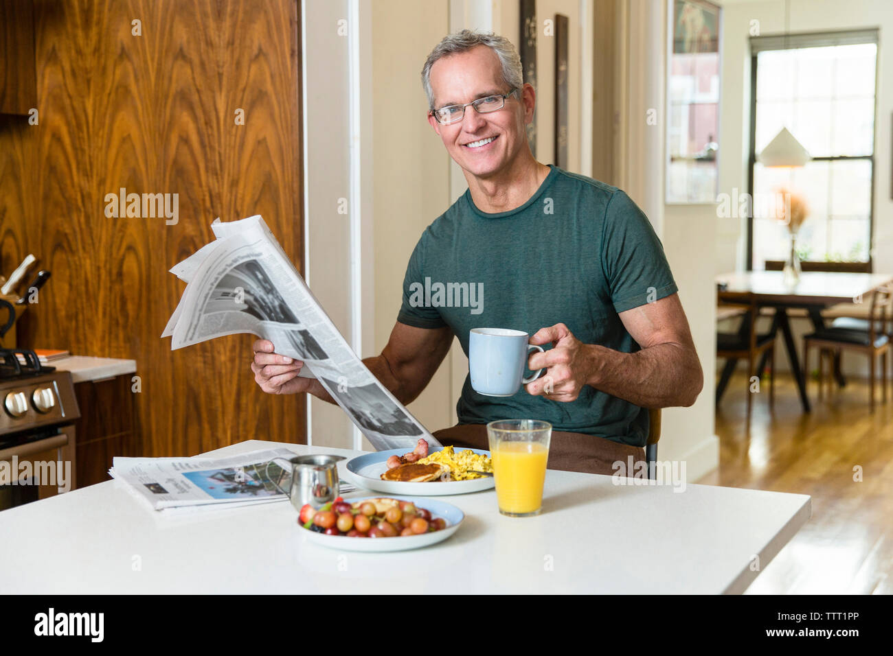 Portrait von lächelnden reifer Mann mit Tasse Kaffee und Zeitung beim Sitzen am Esstisch Stockfoto