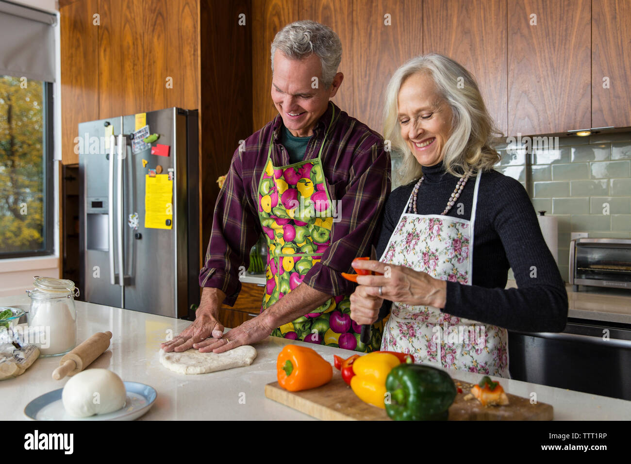 Lächelnde Frau schneiden Paprika, während Mann, Pizza Teig in der Küche zu Hause. Stockfoto