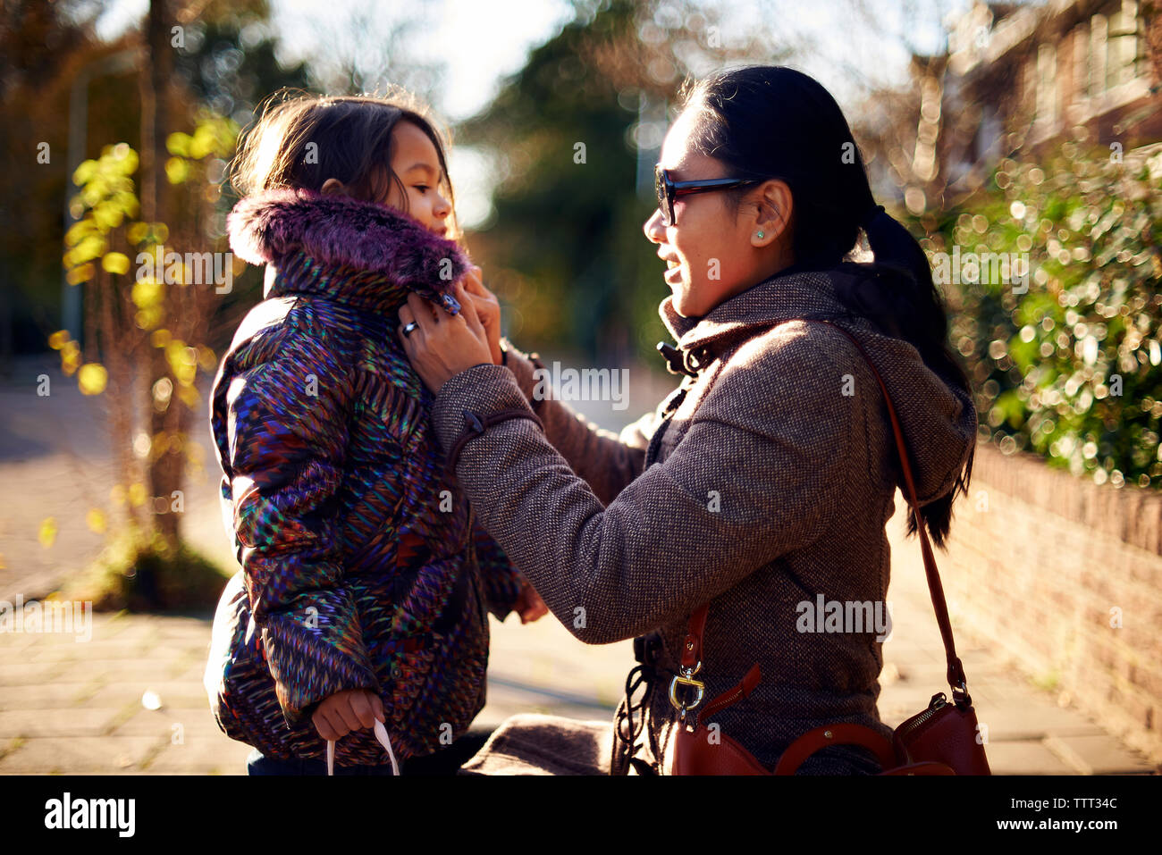Die Mutter hilft der Tochter in das Tragen winter Mantel an Fußweg Stockfoto