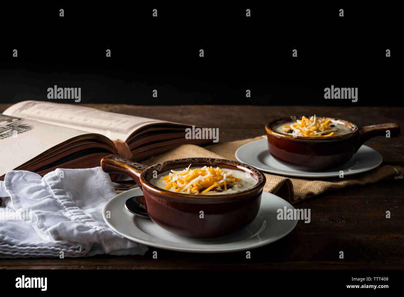 Chowder mit Käse in der Schüssel durch offenes Buch auf Tisch Stockfoto