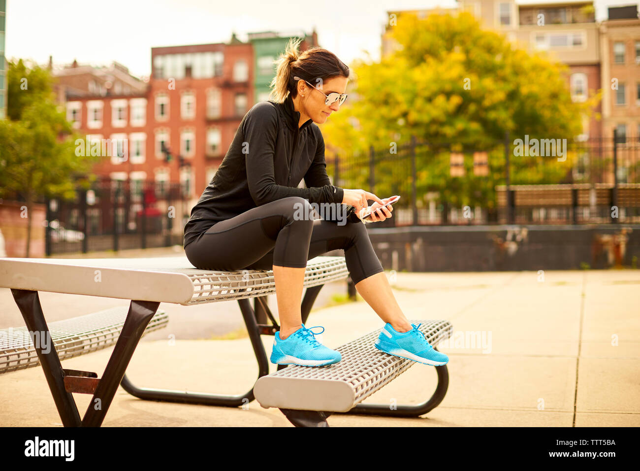 Eine athletische Frau sms beim Sitzen auf einem Picknicktisch in einem Park. Stockfoto