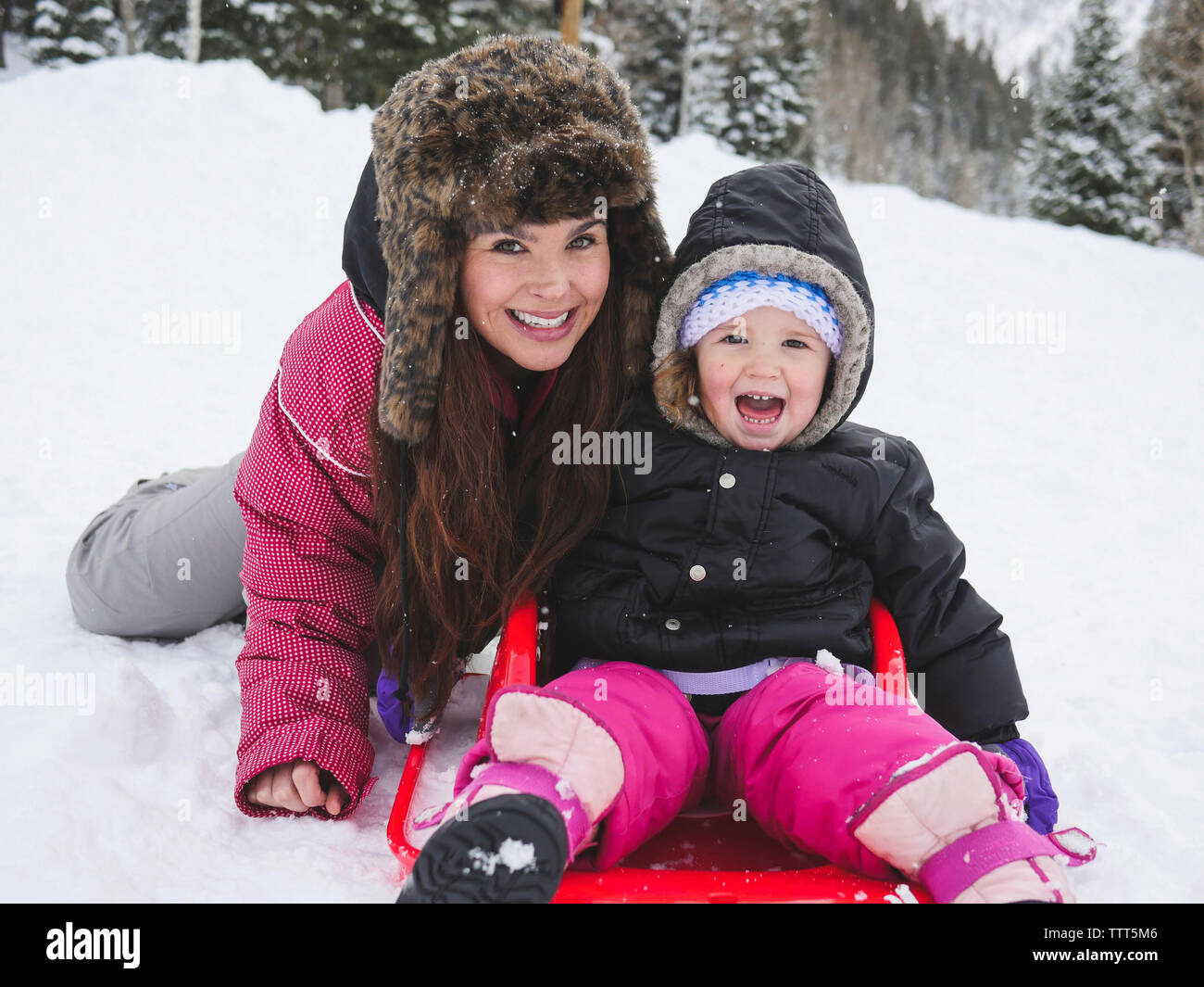 Portrait der glücklichen Mutter mit Tochter sitzen auf schneebedeckten Feld Stockfoto
