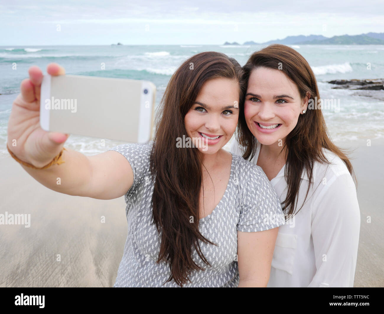 Glückliche Schwestern unter selfie mit Handy beim Stehen am Strand gegen Sky Stockfoto