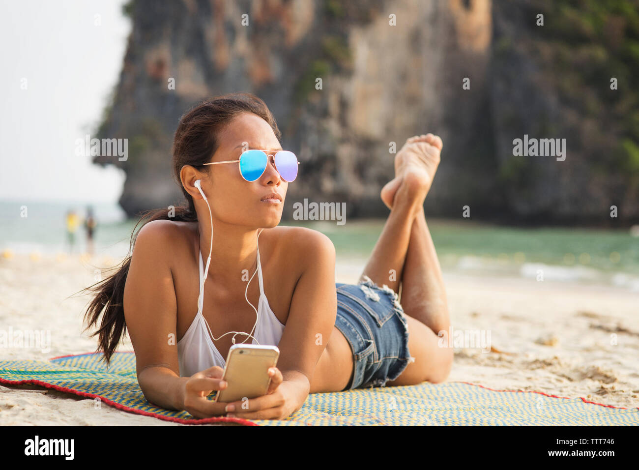 Frau Musik hören durch Smart Phone, während auf Matten am Strand liegen Stockfoto