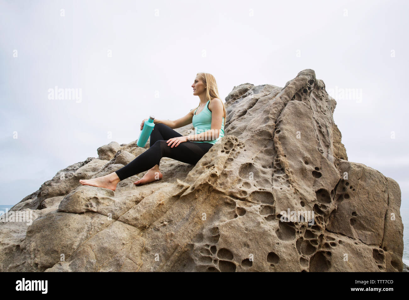Low Angle View der Frau mit Flasche entspannen auf Rock gegen Sky Stockfoto