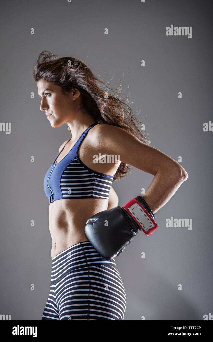 Frau mit Boxhandschuhen weg schauen, während gegen grauen Hintergrund stehend Stockfoto
