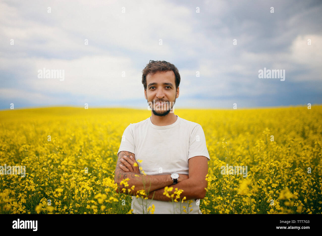 Portrait von zuversichtlich Mann, der Arme in Raps Feld gegen Himmel kreuzte Stockfoto