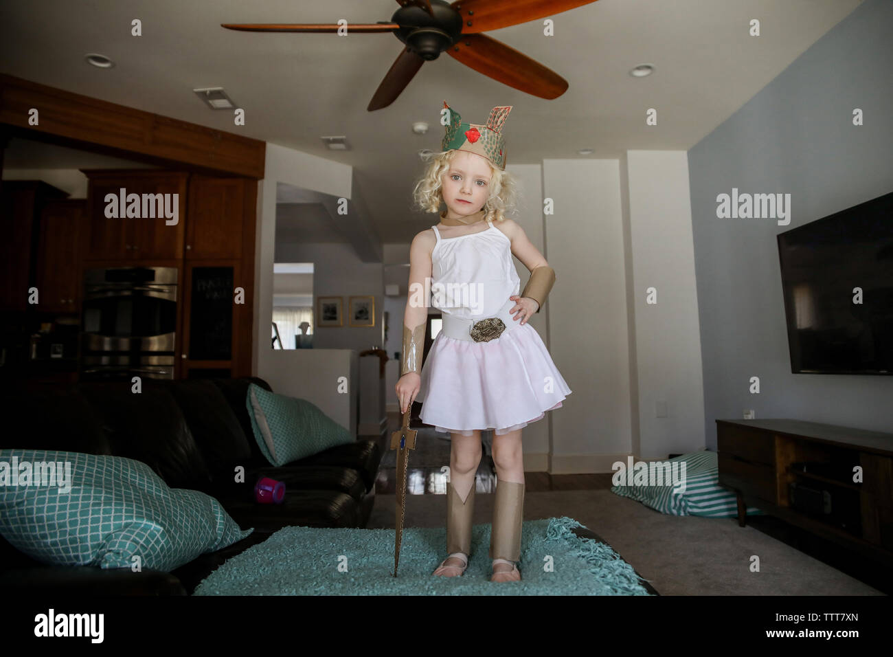 Portrait von Mädchen mit Krone, während Karton Schwert im Wohnzimmer Stockfoto