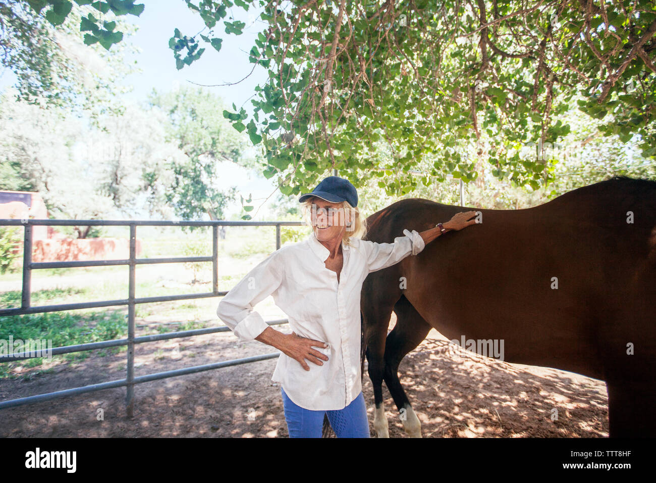 Zuversichtlich senior stehende Frau mit Pferd gegen Baum Stockfoto