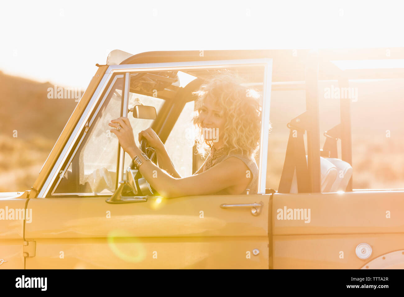 Fröhliche Frau weg schauen, während im Sitzen-Fahrzeug während der sonnigen Tag Stockfoto