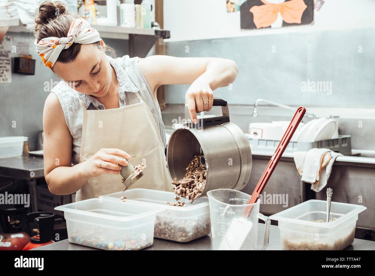 Frau gießen gemahlen Zutaten in Container, während sie Eiscreme an kommerzielle Küche Stockfoto