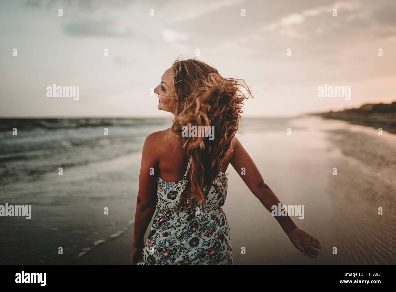 Ansicht der Rückseite des glücklichen Frau zu Fuß am Strand gegen Himmel bei Sonnenuntergang Stockfoto