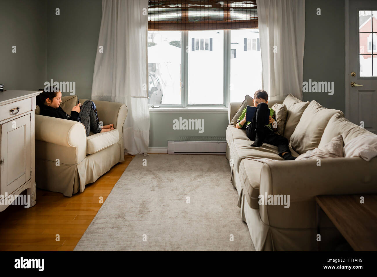 Geschwister verwenden drahtlose Technologie beim Entspannen im Wohnzimmer zu Hause Stockfoto