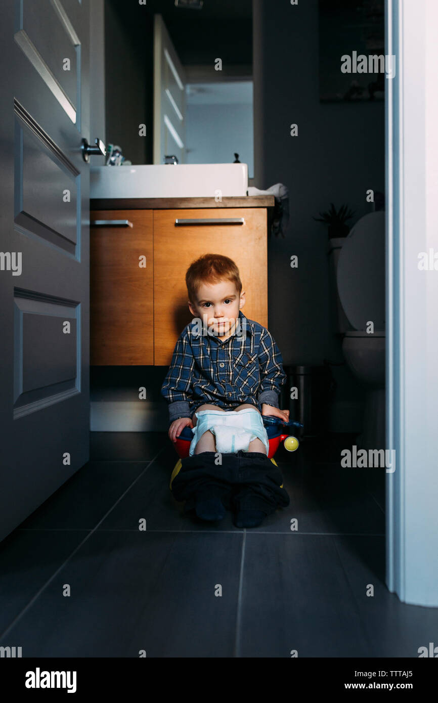 Porträt der jungen Defecating während auf Töpfchen durch die Tür zu Hause gesehen sitzen Stockfoto