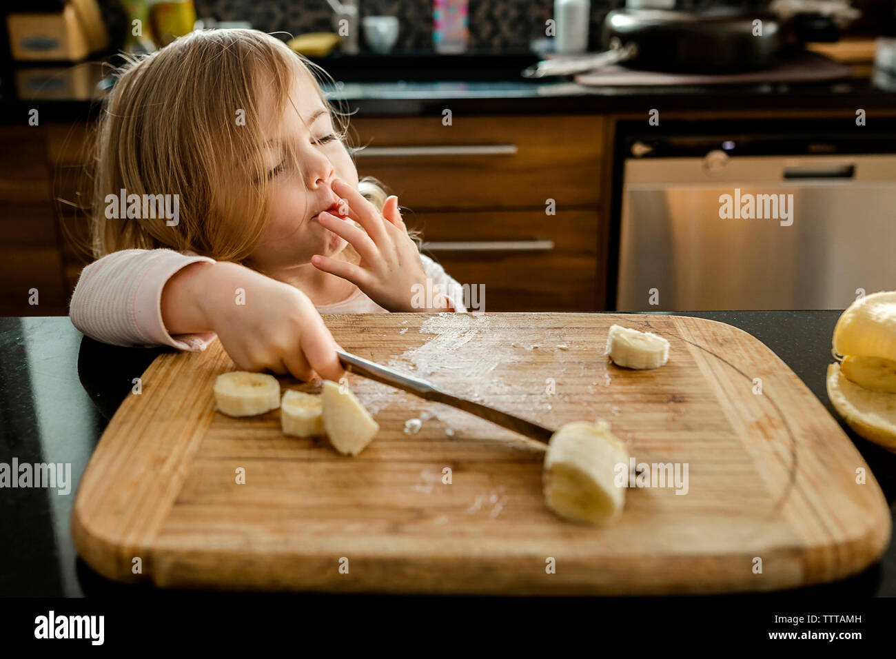 Kleinkind Mädchen schneiden und essen Bananen in der Küche Stockfoto