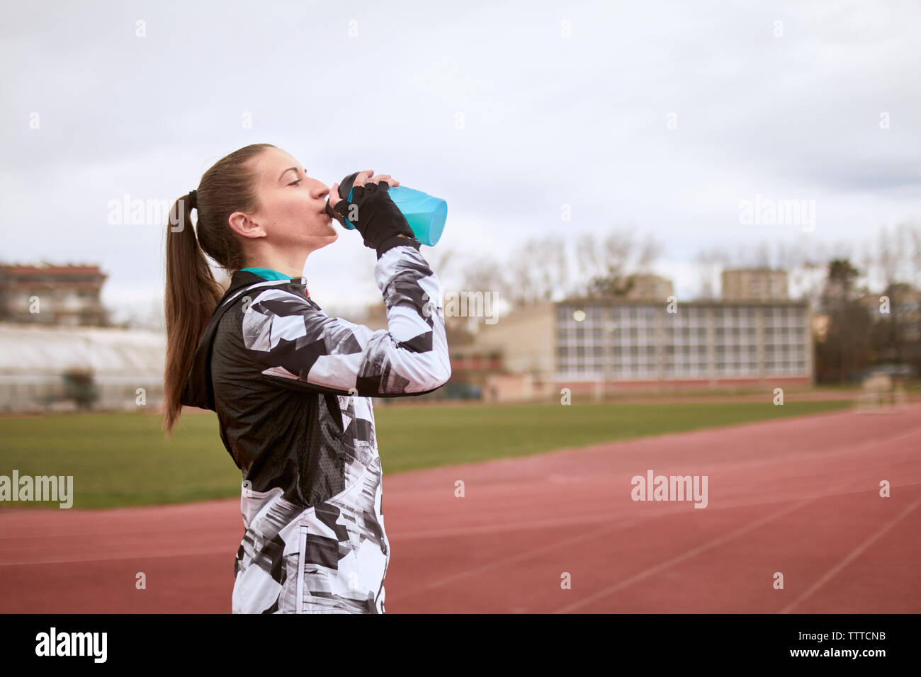 Seitenansicht des Frau trinkt Wasser stehend gegen den Himmel bei Sport Track Stockfoto