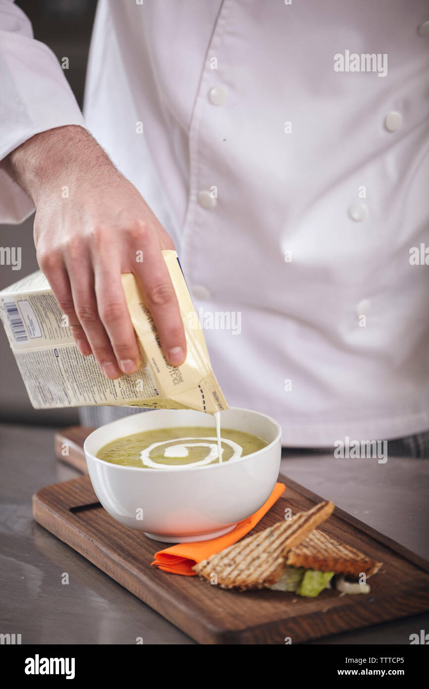 Mittelteil von Chef gießen Creme während der Vorbereitung Matcha Tee mit geröstetem Brot auf schneidebrett an gewerbliche Küche Stockfoto