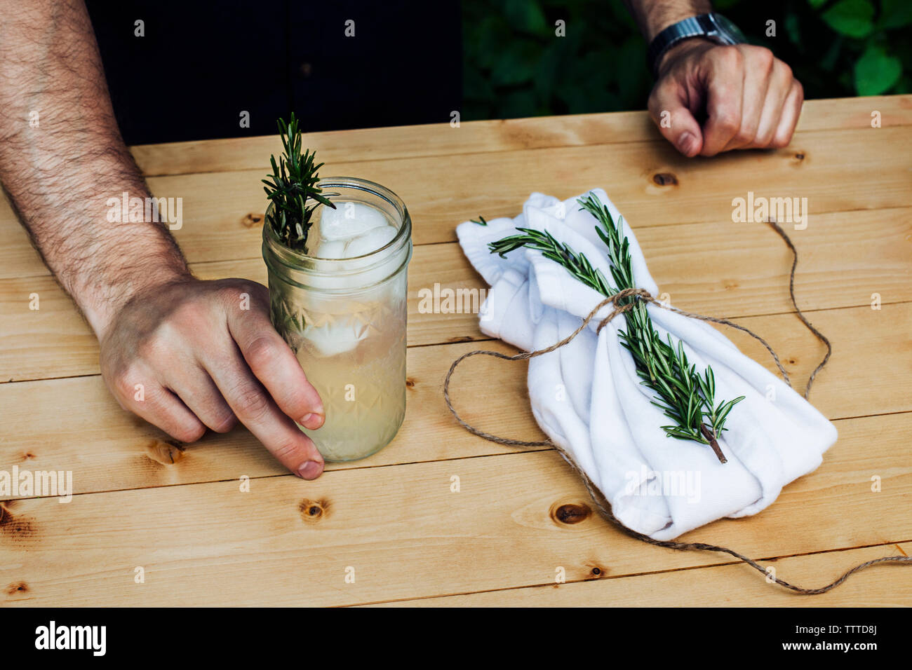 Mittelteil der Mann mit Limonade Glas mit Rosmarin am Tisch Stockfoto