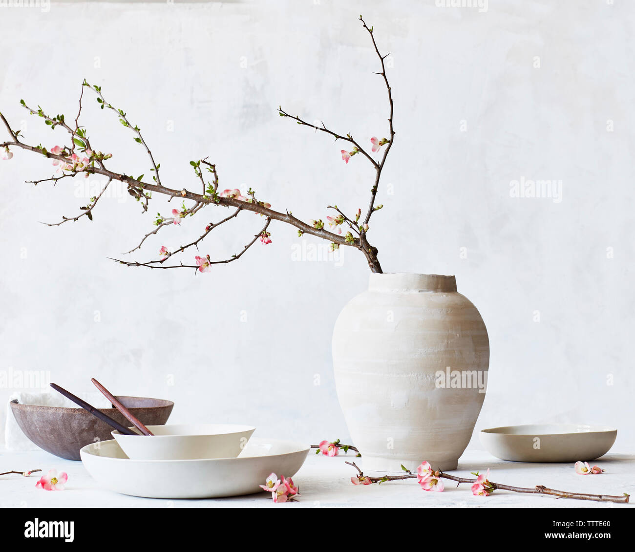 Vase mit Schüsseln und Teller am Tisch gegen die Wand Stockfoto