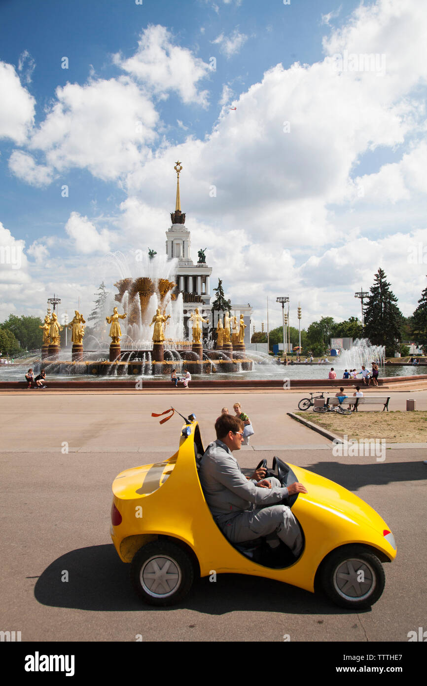 Russland, Moskau. Russland, Moskau. Vistiors reiten ein gelbes Auto vor den Völkern Freundschaft Springbrunnen auf dem Allrussischen Ausstellungszentrum. Stockfoto