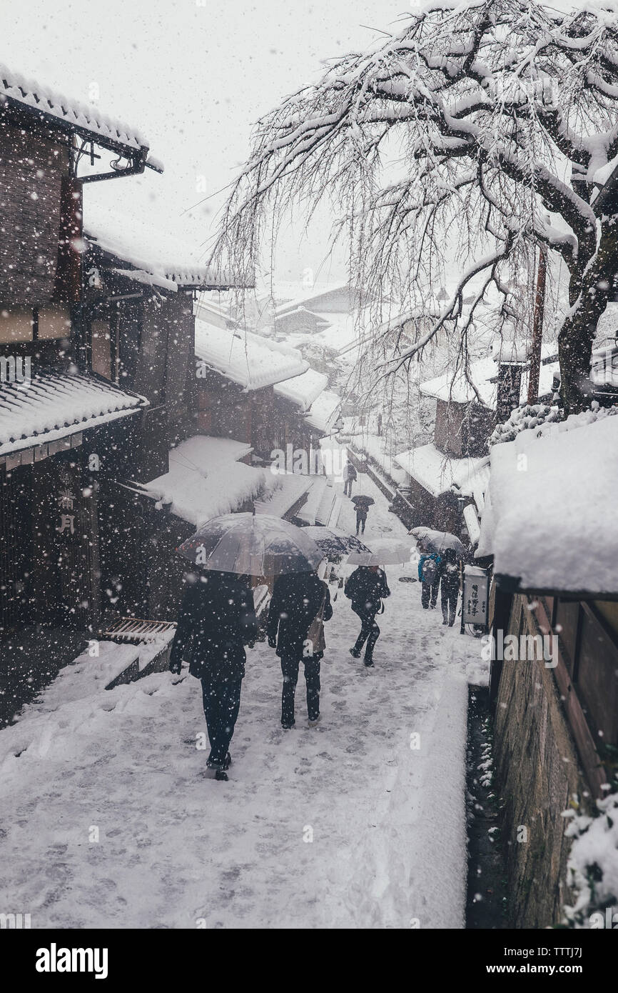 Hohe Betrachtungswinkel von Menschen mit Regenschirm beim Gehen auf Wanderweg in Stadt bei Schneefall Stockfoto