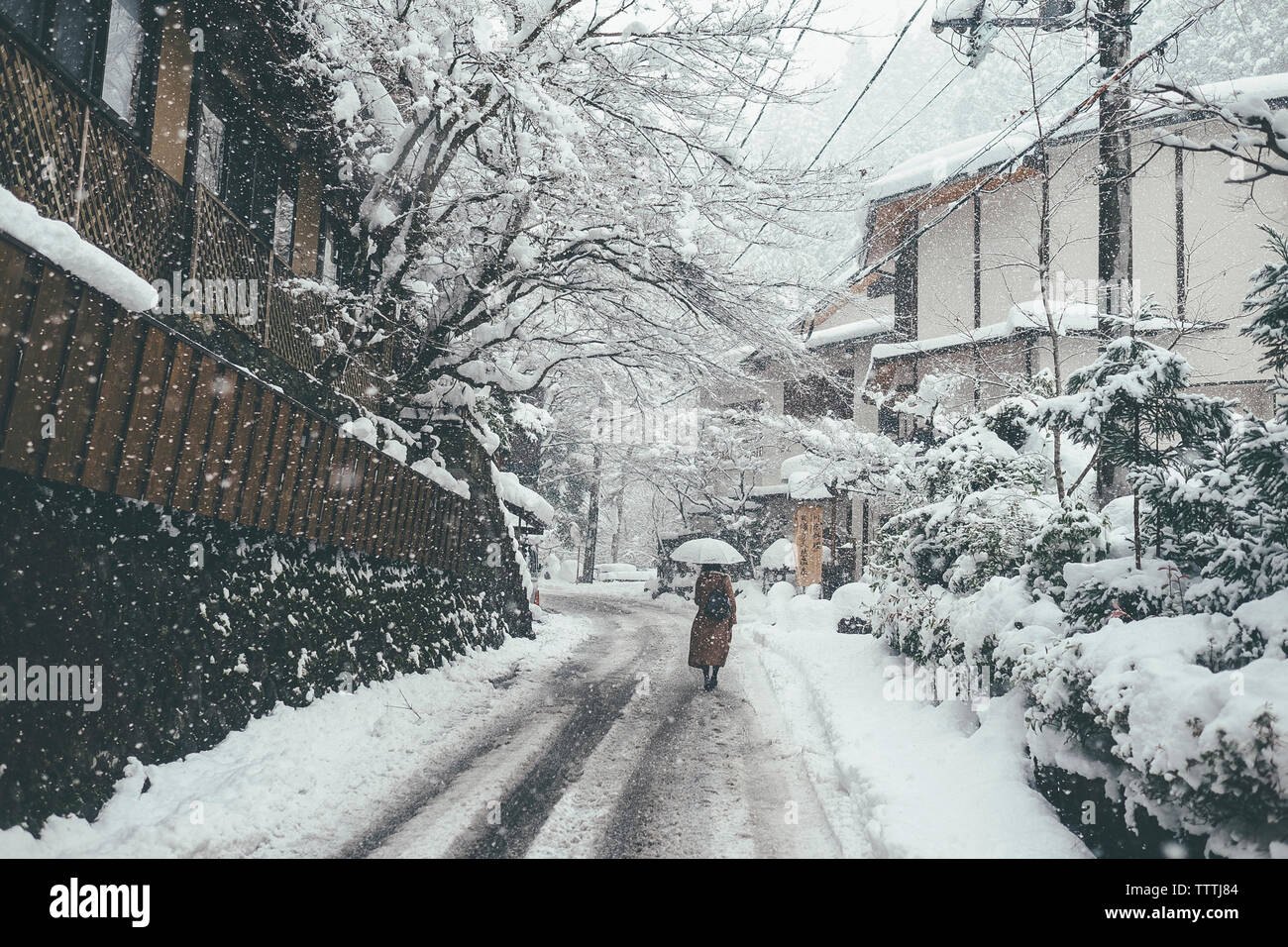 Ansicht der Rückseite Frau mit Regenschirm beim Gehen auf schneebedeckten Straßen bei Schneefall in der Stadt Stockfoto