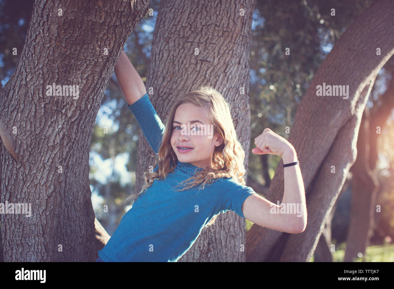 Portrait von zuversichtlich Mädchen flexing Muskeln beim Hängen am Baum im Park Stockfoto
