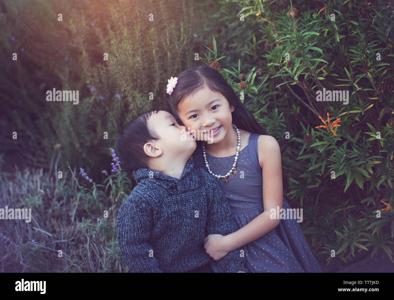 Portrait der netten Schwester mit Bruder sie zu küssen gegen Pflanzen im Park Stockfoto