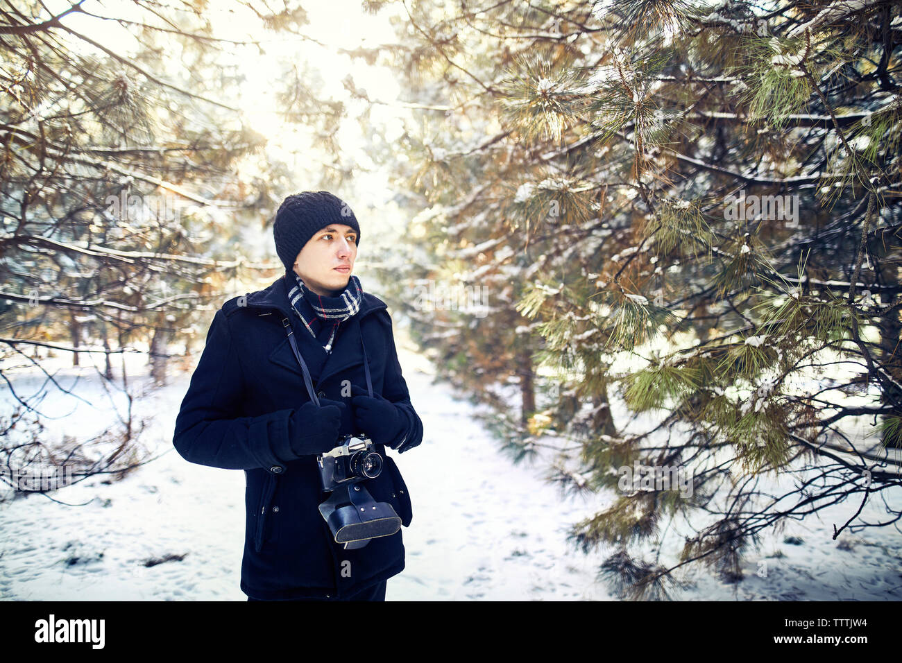 Junger Mann mit Vintage Kamera mit schwarzen warme Kleidung inmitten von Wald im Winter Stockfoto