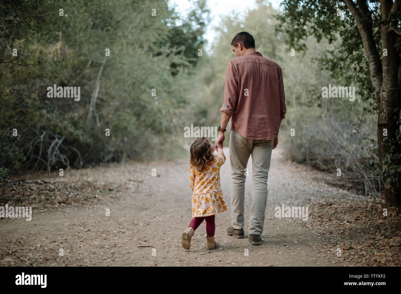 Hintere Ansicht von Vater und Tochter halten sich an den Händen beim Gehen auf die unbefestigte Straße Stockfoto