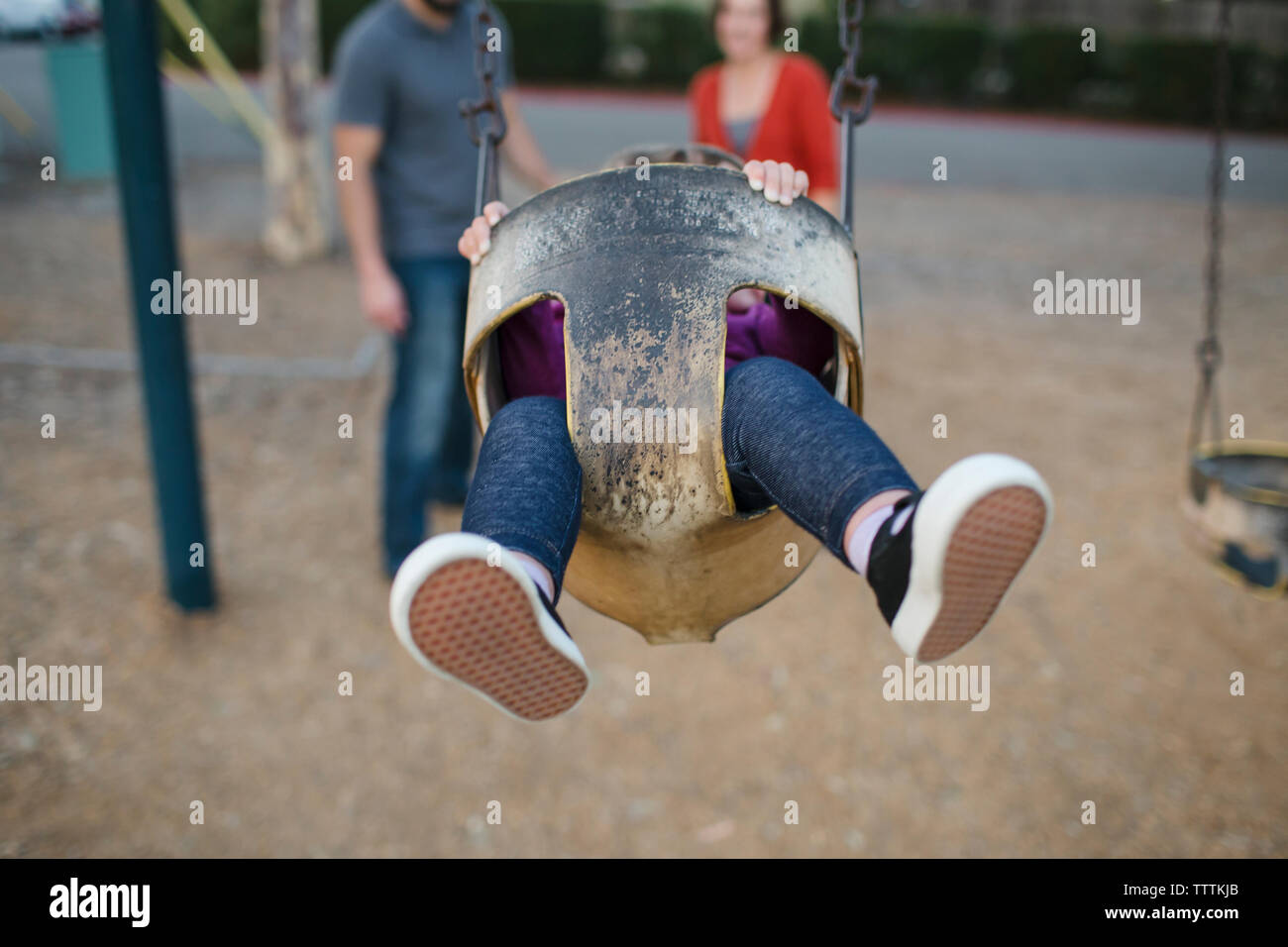 Tochter schwingen auf Spielplatz mit Eltern im Hintergrund stehend Stockfoto