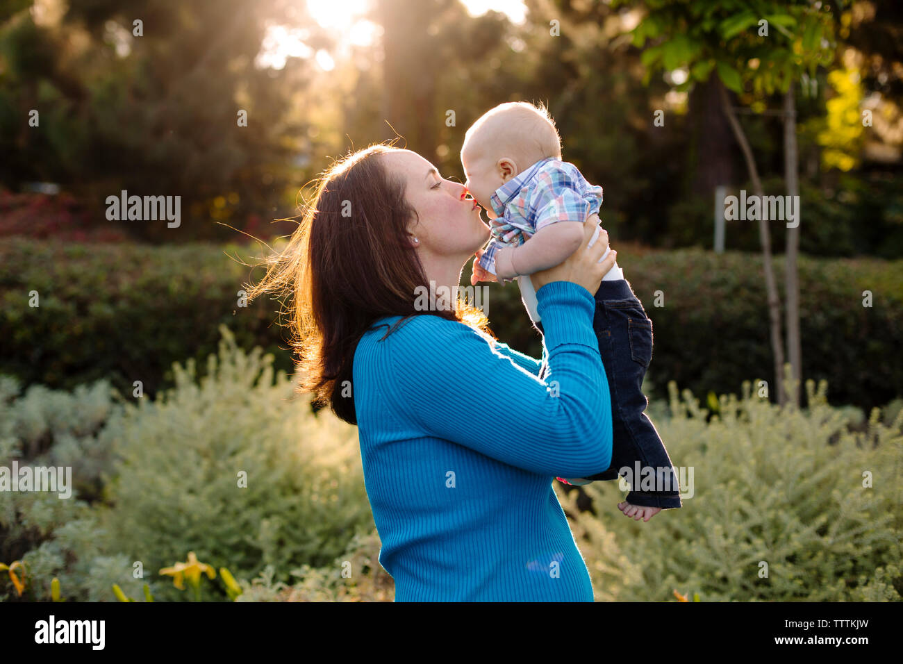 Seitenansicht der Mutter küssen Sohn beim Stehen von Pflanzen Stockfoto