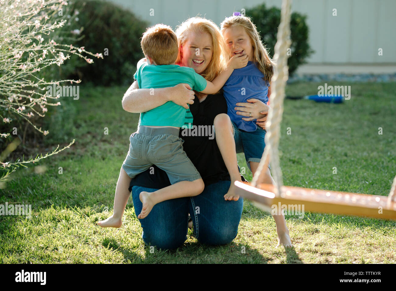 Glückliche Mutter, der Kinder während kniend an der Front Yard Stockfoto