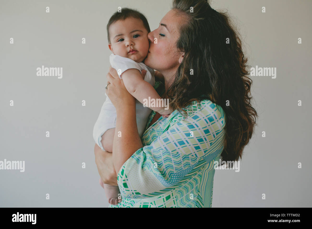 Seitenansicht der Mutter küssen Sohn beim Stehen vor grauem Hintergrund Stockfoto