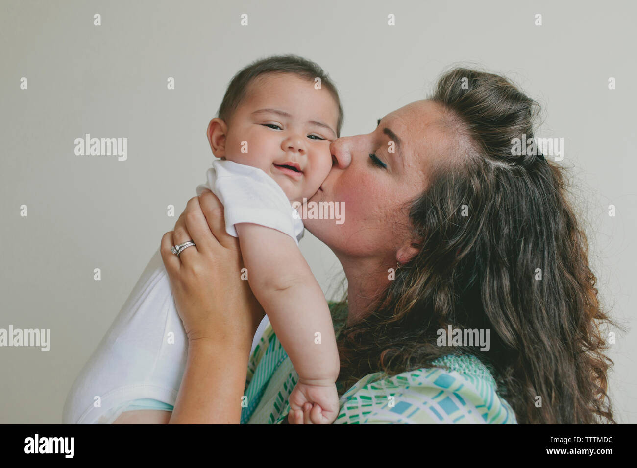 Mutter küssen Sohn beim Stehen vor grauem Hintergrund Stockfoto