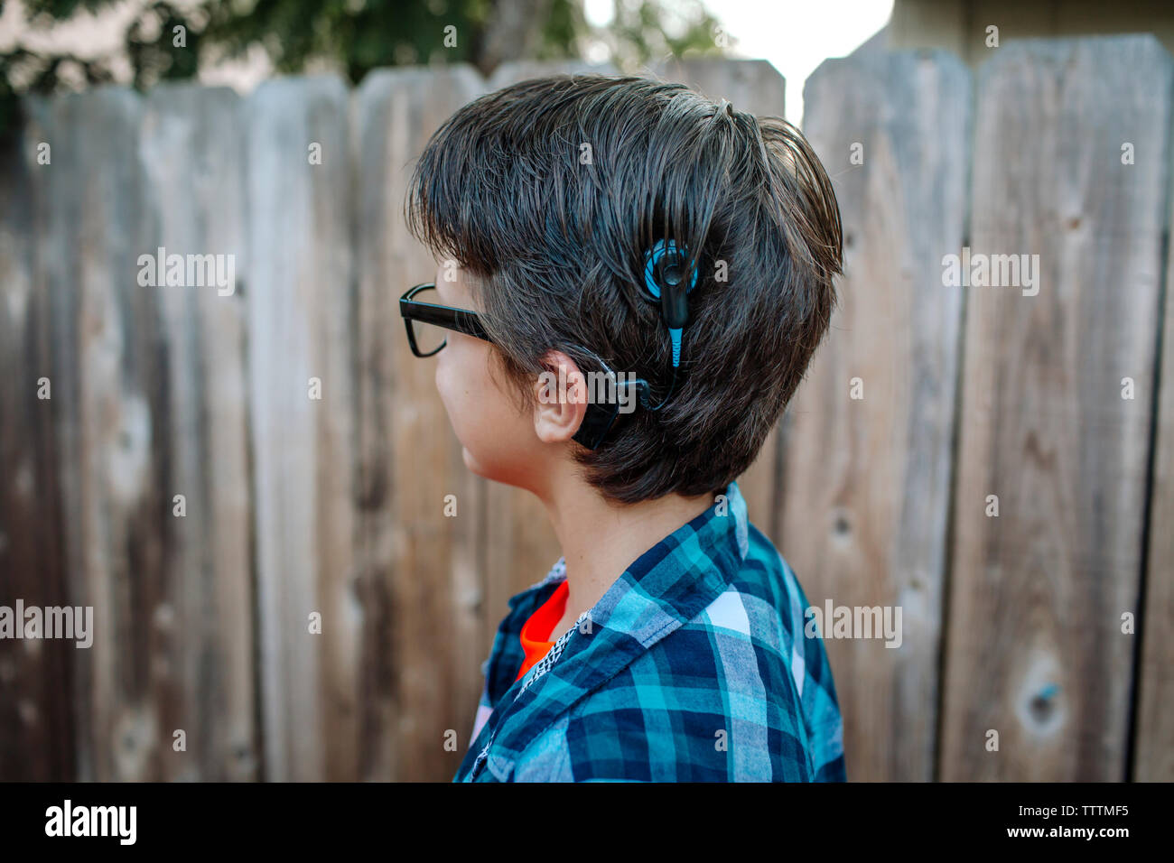Seitenansicht des Jungen mit Anhörung Luft gegen Holzzaun im Hof stehend Stockfoto