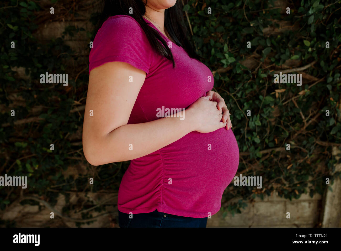 Mittelteil der schwangeren Frau, die von den Pflanzen im Garten Stockfoto