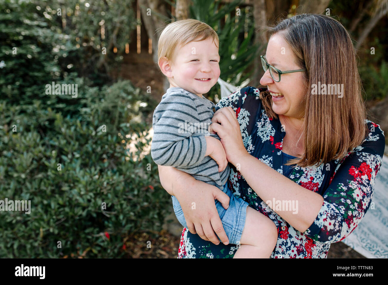 Fröhliche Mutter kitzeln niedlichen Sohn, während ihm im Park tragen Stockfoto