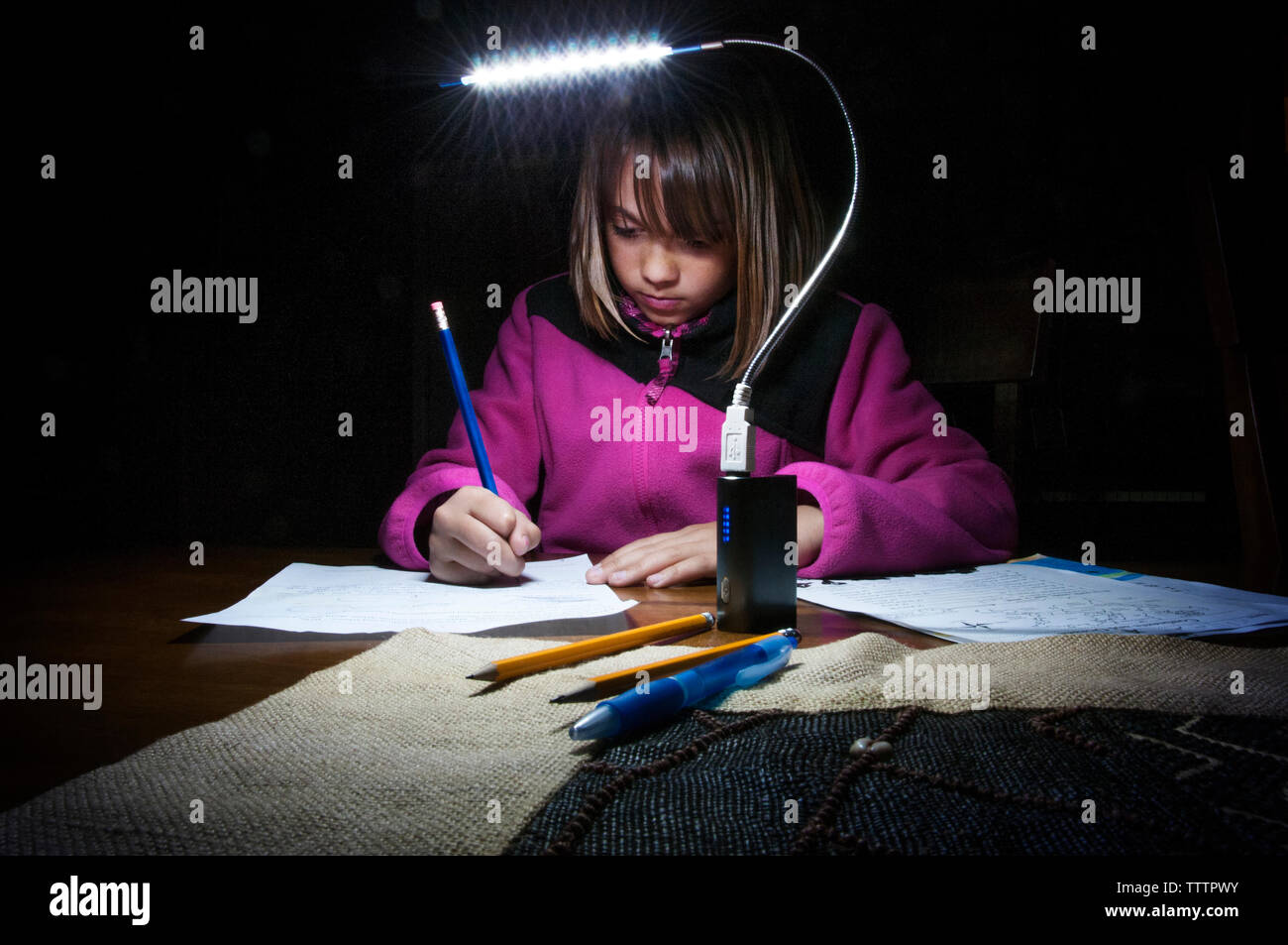 Mädchen studieren durch elektrische Lampe am Tisch in der Dunkelkammer zu Hause Stockfoto