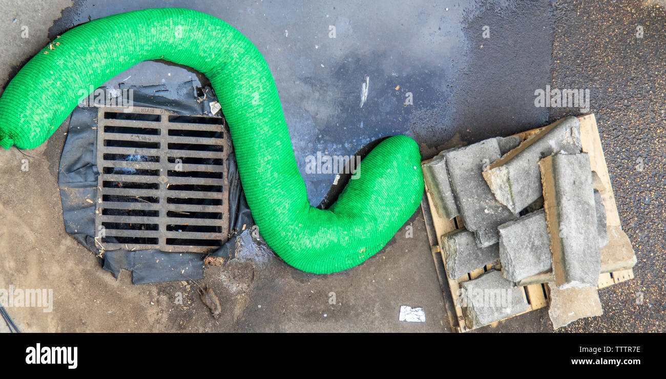 Konkrete Bausteine auf einer Holzpalette und einem grünen Kunststoff Wurst geformte Rollen neben einem Sturm Wasser ablassen. Stockfoto