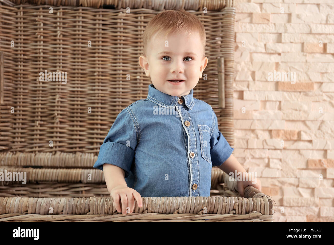 Stilvolle baby boy in Jeanshemd in einem Weidenkorb auf einem Stein Wand  Hintergrund. Fashion Concept Stockfotografie - Alamy