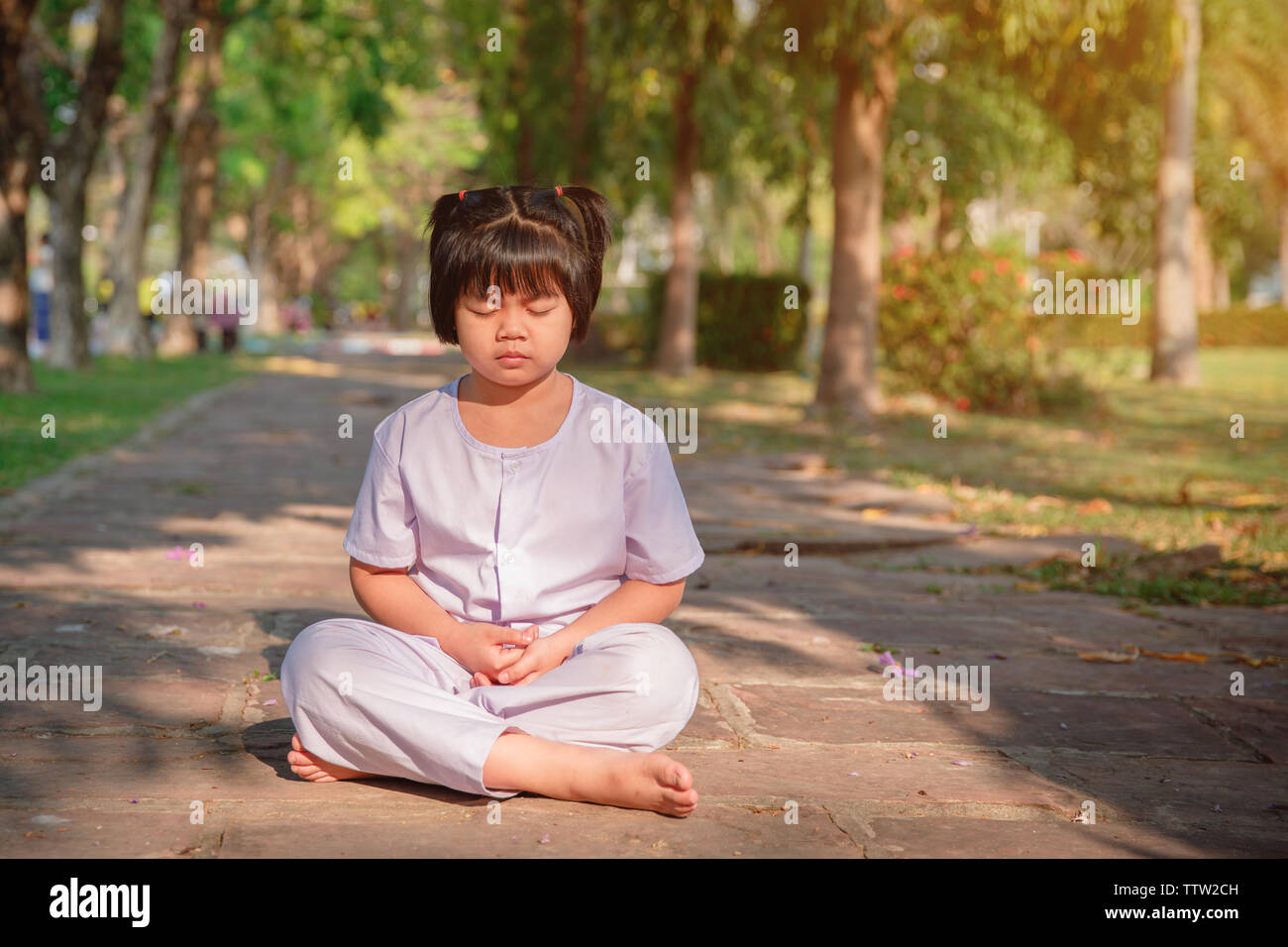 Asiatische Kinder niedlich oder Kind Mädchen sitzen für die Meditation mit Frieden und im Garten Pavillon auf der Tempel oder die Kirche entspannen und tragen weiße Kleid mit Sonnenlicht o Stockfoto