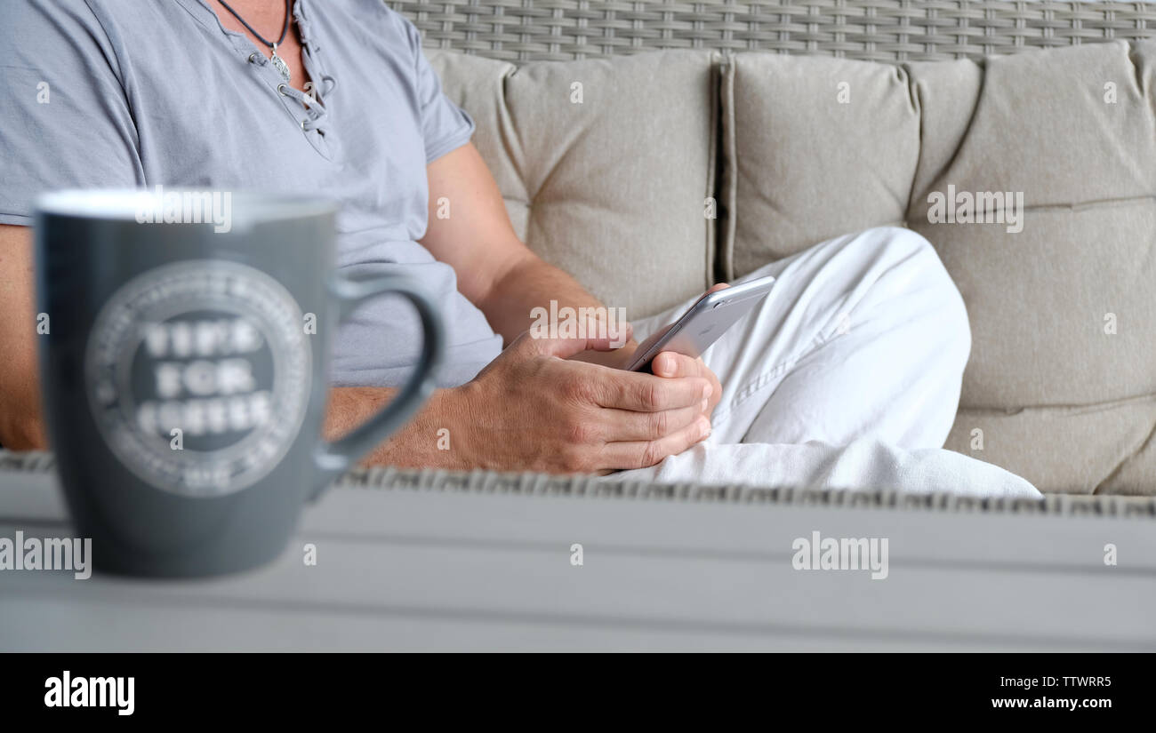 Mann in Freizeitkleidung auf einem Sofa zu Hause sitzen Sms eine Nachricht auf seinem Handy Stockfoto
