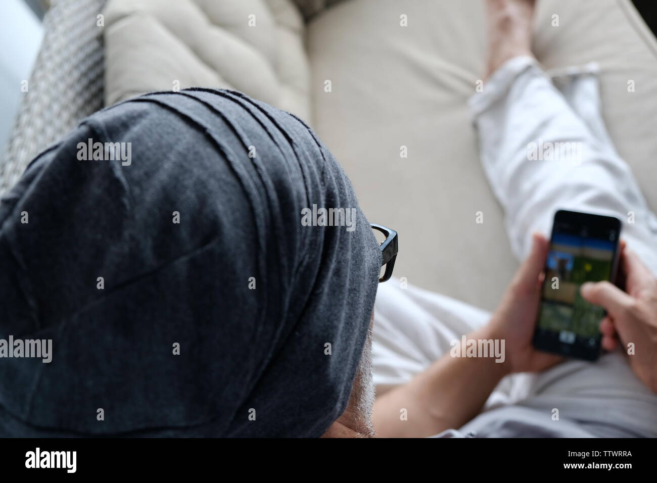 Mann in Freizeitkleidung auf einem Sofa zu Hause sitzen Sms eine Nachricht auf seinem Handy Stockfoto