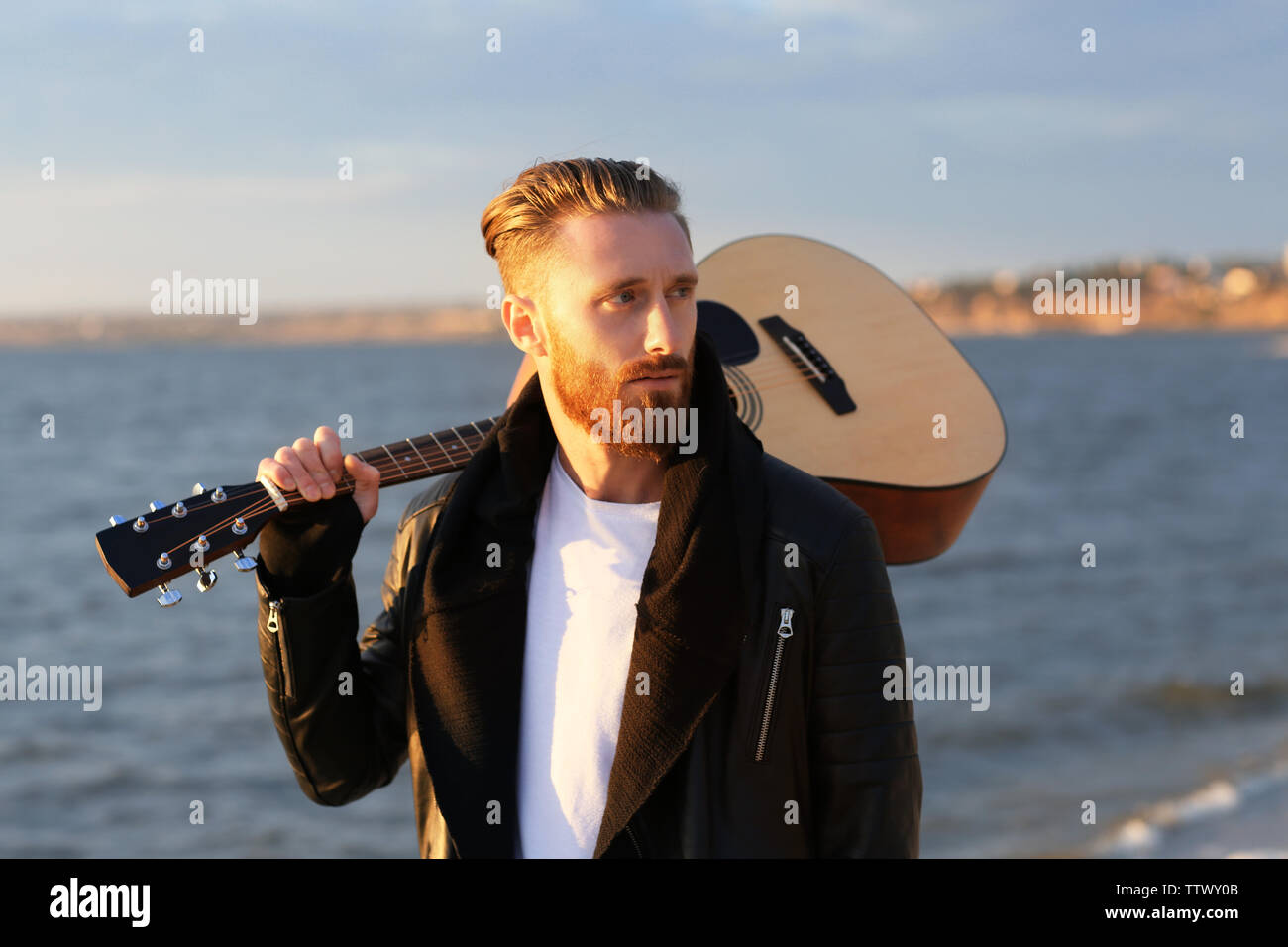 Stattlicher Mann mit Gitarre am Strand Stockfoto