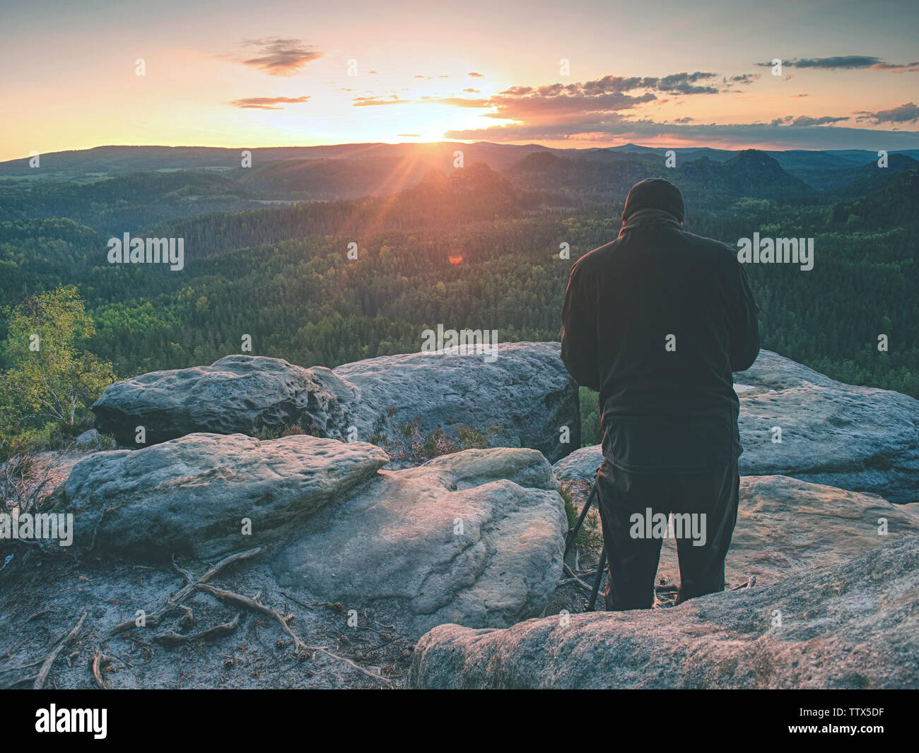 Fotograf mit Stativ auf einer Klippe und Denken. Verträumt neblige Landschaft orange misty Sonnenaufgang in einem schönen Tal, unten Stockfoto